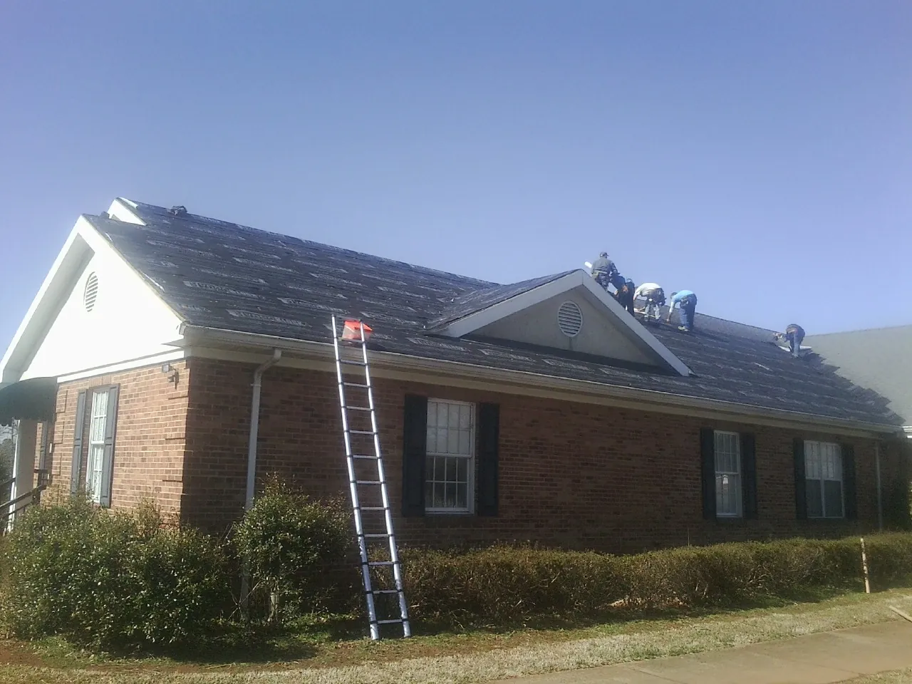Crew tearing shingles off a brick ranch roof with a ladder set — Emergency Roof Repair work by our crew in Oak Brook