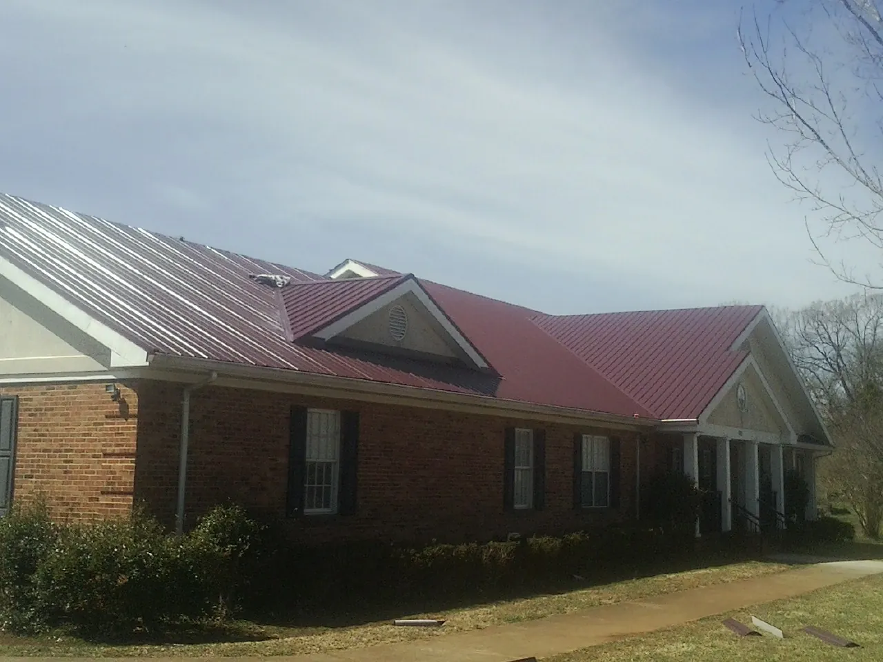 Red metal roof with gabled entries on a long brick building, from a Hail Damage Roof Repair job in Oak Brook