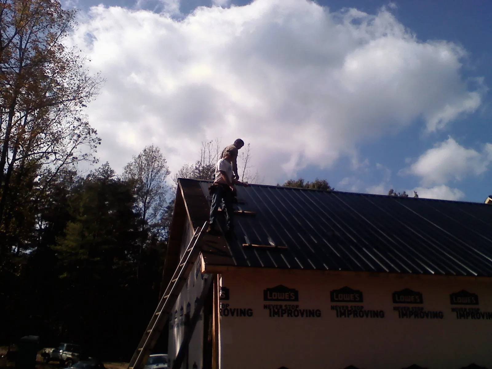 Roofer fastening dark metal panels high against a cloudy sky, from a Roof Inspection job in Oak Brook